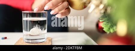 Donna gettando la pillola solubile effervescente in vetro di acqua a. casa vicino closeup albero di natale Foto Stock