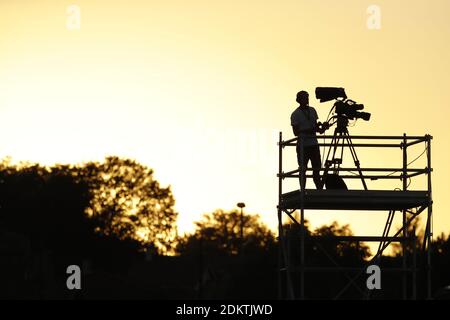 Cameraman su una piattaforma che filma una partita di calcio su uno stadio, con una luce gialla sullo sfondo Foto Stock