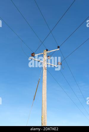 Pali telegrafici in legno con fili e isolatori contro un trasparente sfondo blu cielo Foto Stock