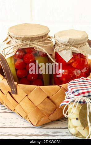 Pomodori fatti in casa conserve in vasi di vetro in bianco cesto di vimini su sfondo di legno. Foto Stock