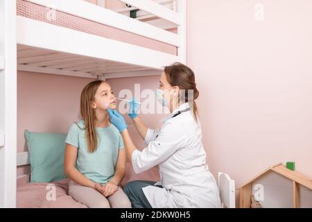 Pediatra che prende un campione di prova del muco nasale da bambina di età elementare naso che esegue la procedura di test del virus respiratorio a casa durante il coronavirus Foto Stock