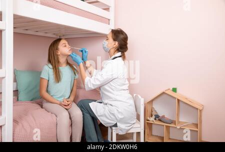 Pediatra che prende un campione di prova del muco nasale da bambina di età elementare naso che esegue la procedura di test del virus respiratorio a casa durante il coronavirus Foto Stock