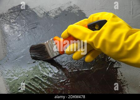 Mano con spazzola in un guanto di gomma giallo, vernici con vernice nera. Il concetto di design creativo Foto Stock