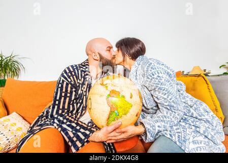 felice coppia di un uomo baldacchino hipster e bruna caucasica donna che baciano e tiene terra globo seduto comodo su un couch.travel plan,togethernes Foto Stock