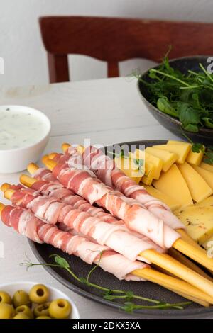 Pane grissini con pancetta, diversi tipi di formaggio e germogli di piselli, salsa e olive su fondo bianco di legno Foto Stock