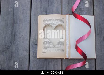 Vista dall'alto di un libro le cui pagine sono tagliate a forma di cuore con un filo ondulato rosso. Sfondo di legno. San Valentino 2021. Foto Stock