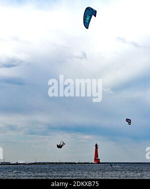 Un kite-boarder windsurf in una giornata parzialmente nuvolosa con un faro sullo sfondo Foto Stock
