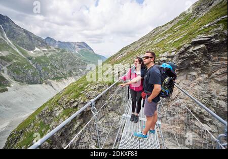 Coppia di turisti che viaggiano nelle Alpi svizzere, uomo e donna che si trovano su un ponte godendo della natura intorno a loro, incredibili viste sono mozzafiato Foto Stock