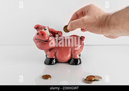 Male hand throws a coin into a piggy bank and euro coins on a white background. Keeping money and investment concept. Selective focus Stock Photo