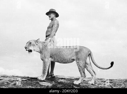 George Adamson in piedi su uno sperone roccioso con Elsa la leonessa. Una di una serie di immagini originali della raccolta di foto libere nata da Joy Adamson, per la maggior parte prese dal 1940 all'inizio degli anni '60 in Kenya. Foto Stock