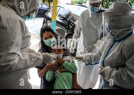 Medan, Indonesia. 16 Dic 2020. Gli operatori sanitari che indossano tute per dispositivi di protezione individuale (PPE) sono visti convincere un ragazzo a prendere il test del tampone a Medan, Sumatera del Nord.mentre i casi di Covid19 aumentano a Medan, gli operatori sanitari prendono i bambini attraverso test con tampone e scansioni di temperatura per frenare la diffusione del coronavirus. Credit: SOPA Images Limited/Alamy Live News Foto Stock