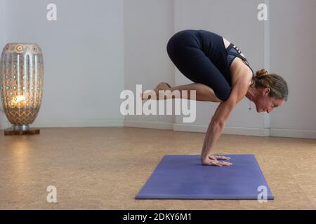 Donna forte in bakasana yoga posa in piedi sulle mani con le gambe ripiegate solo in studio. Yogi femminile flessibile che pratica la serie intermedia di ashtanga Foto Stock