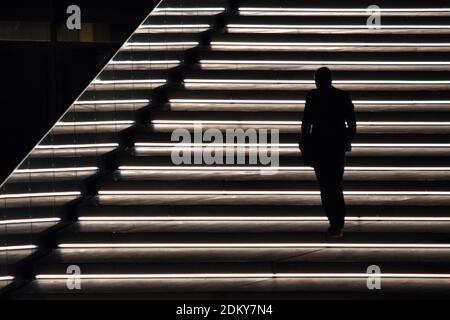 Silhouette di uomo che cammina giù su una scala illuminata di notte Foto Stock