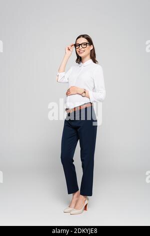 sorridente giovane donna d'affari incinta in occhiali isolati su grigio Foto Stock