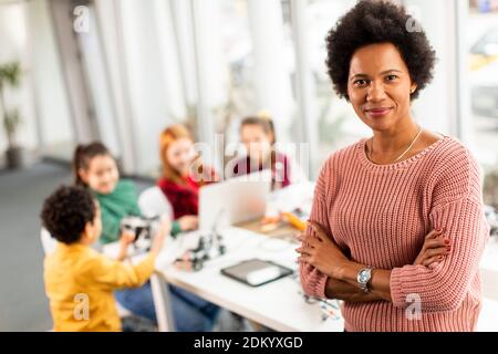 Smily African American insegnante di scienza femminile con gruppo di bambini programmazione di giocattoli e robot elettrici in classe robotica Foto Stock