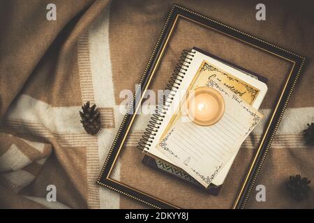 Composizione accogliente con cornice in legno, libri e candela su sfondo calde plaid e coni, tema inverno autunno copia spazio foto Foto Stock