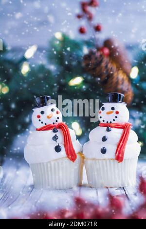 Due cupcake natalizi ghiacciati di Snowman con naso di carota, cappello di santa e sciarpa. Messa a fuoco selettiva con primo piano e sfondo sfocati. Foto Stock