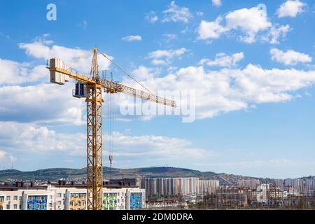 Gru o torre gialla con cabina in altezza, sullo sfondo di un cielo azzurro e di un paesaggio urbano. Foto Stock