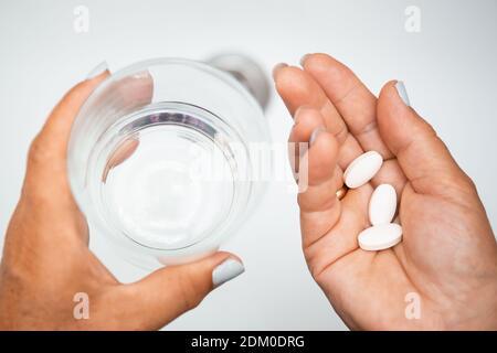 Donna anziana mano con pillole compresse di medicina e un bicchiere d'acqua contro lavelli bianchi con acqua dolce. Donna anziana che prende le pillole a casa, closeup. D Foto Stock