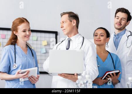 Personale ospedaliero multietnico con tablet digitale e notebook sorridenti lavorare in clinica Foto Stock