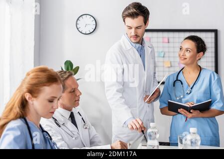 Personale ospedaliero multietnico con notebook e tablet digitali che lavorano insieme in ospedale Foto Stock