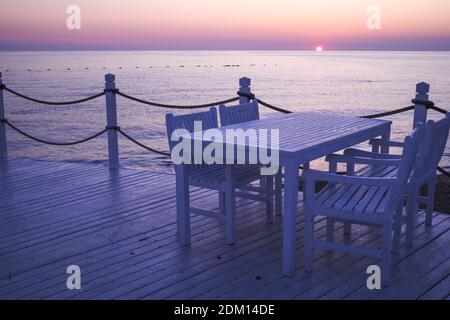 Sunrise, Sunset Purple e Orange Light si riflettono sul tavolo e sulla sedia in legno bianco leggermente bagnato al molo di Antalya Turchia. Foto Stock