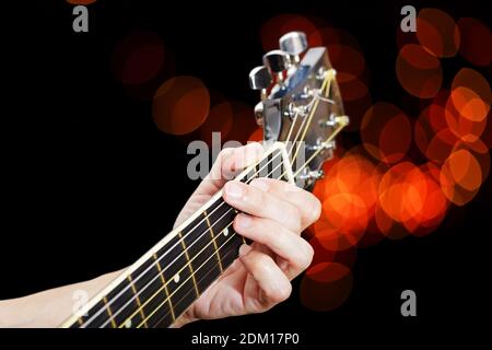 Uomo che suona su chitarra acustica. Avvicinare le dita sul collo della chitarra contro le luci del bokeh sfocate sullo sfondo. Messa a fuoco superficiale. Foto Stock