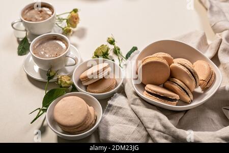 Deliziosi maccheroni francesi e caffè froso in tazze bianche. Dessert ancora vita su sfondo beige. Primo piano Foto Stock