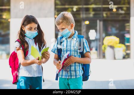 Bambini in maschere protettive all'aperto guardando i loro copybook Foto Stock