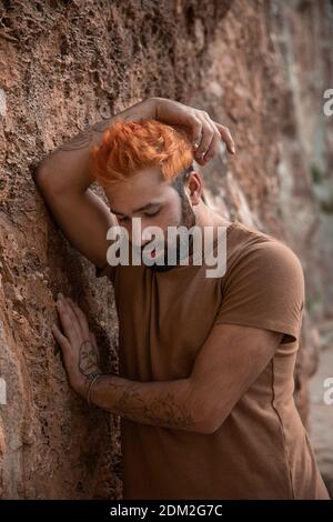 Ritratto di giovane triste uomo con i capelli arancioni appoggiati un muro di pietra Foto Stock