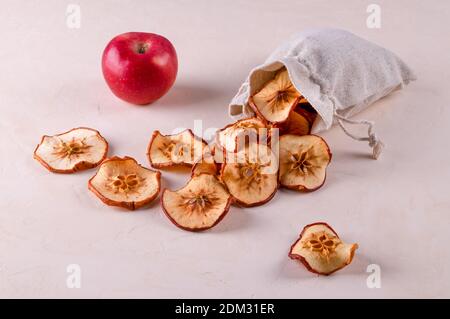 Fette di mele di frutta secca in un sacchetto eco-friendly e una mela rossa matura giacciono su una superficie leggera. Prodotti utili, protezione ambientale, riciclaggio Foto Stock