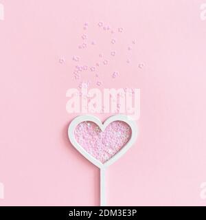Bacchetta magica a forma di cuore con sequine di stelle su un rosa sfondo pastello Foto Stock