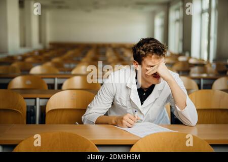 Medico che compila un documento, che guarda esausto, stanco. Medico che scrive un esame di opinion.Medicine, medico che prende il test evalu Foto Stock