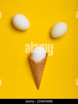 Uova di pollo bianche in una cialda tromba su sfondo giallo, vista dall'alto, piatto, tendenza minimalista Foto Stock