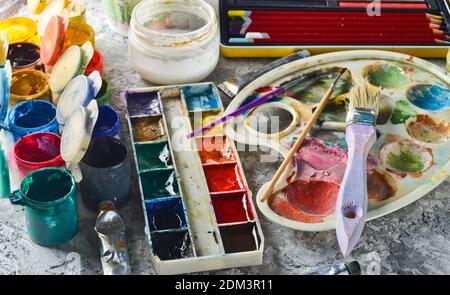 Strumenti artistici per disegnare dipinti su sfondo grigio di cemento. Palette, gouache, olio di vernice, pennelli, pastelli colorati, pastello, matite colorate. Foto Stock