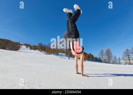 Woman doing hand stand on a ski track in sunlight Stock Photo