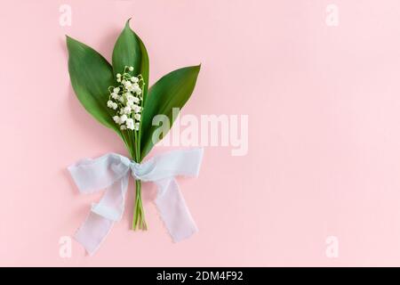 Bouquet di gigli della valle con foglie verdi legate con un nastro su sfondo rosa pastello Foto Stock