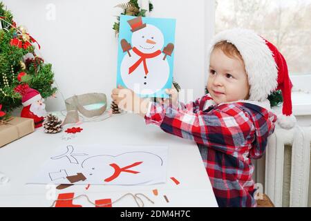 bambina in cappello di santa fa un'applicazione di carta colorata con pupazzo di neve. il concetto di creatività dei capretti di inverno. Foto Stock