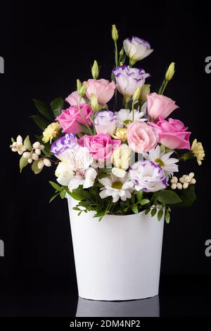 bouquet di fiori di rose, lisianthus, margherite, crisanthemi in una scatola rotonda bianca su uno sfondo nero a specchio con un riflesso Foto Stock