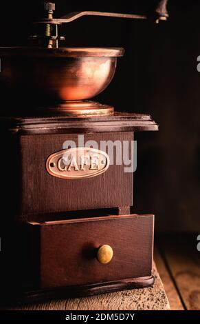 Macinacaffè d'epoca, in tonalità scure su rustico sfondo in legno. Vecchia attrezzatura per la preparazione del caffè. Messa a fuoco selettiva. Profondità di campo poco profonda. Foto Stock