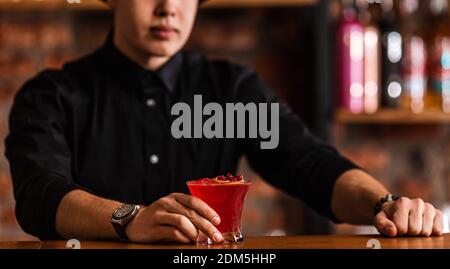 Deliziate il cocktail di mirtilli rossi con cubetti di ghiaccio. Il barman esperto crea un cocktail di mirtilli al bar. Bevanda alcolica rossa. Foto Stock