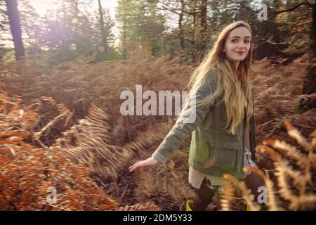 Una giovane donna naturalmente bella (20 anni) corre attraverso le felci autunnali divertirsi in un ambiente forestale con un senso di movimento in una giornata di sole. Foto Stock