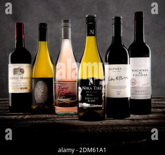 Un mix di sei bottiglie di vino rosso e bianco sparate nello studio su uno sfondo grigio in tela e su una base in legno. Foto Stock