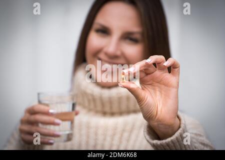 Giovane bella donna sorridente che tiene la pillola di olio di pesce e un bicchiere d'acqua Foto Stock