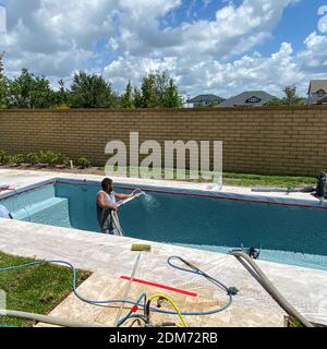 Orlando, FL USA - July7, 2020: Un lavoratore da una società di finitura piscina spruzzando intonaco finitura all'interno di una piscina in Florida. Foto Stock