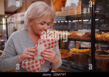 Bella donna anziana che acquista pane fresco presso il negozio di panetteria locale, odore gustoso pane fresco di pane Foto Stock