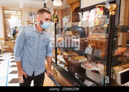 Uomo che indossa una maschera medica protettiva, shopping in panetteria durante la quarantena pandemica del coronavirus Foto Stock