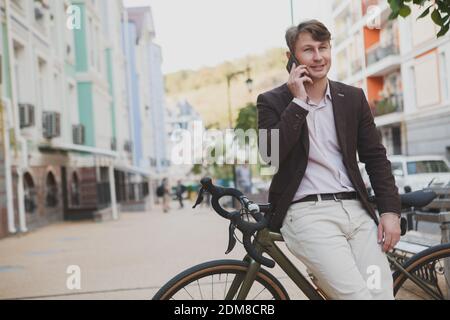 Affascinante uomo d'affari maturo sorridente, parlando al telefono, appoggiandosi sulla sua bicicletta Foto Stock
