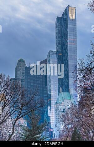 Vista degli edifici alti e moderni di Central Park South dall'interno di Central Park in autunno con fogliame in primo piano e cielo di luna sullo sfondo. Foto Stock