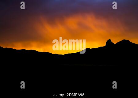 Tramonto brillante attraverso la fascia della pioggia e le nuvole sopra la silhouette nera della montagna all'orizzonte. Tramonto nel deserto dall'Arizona. Foto Stock